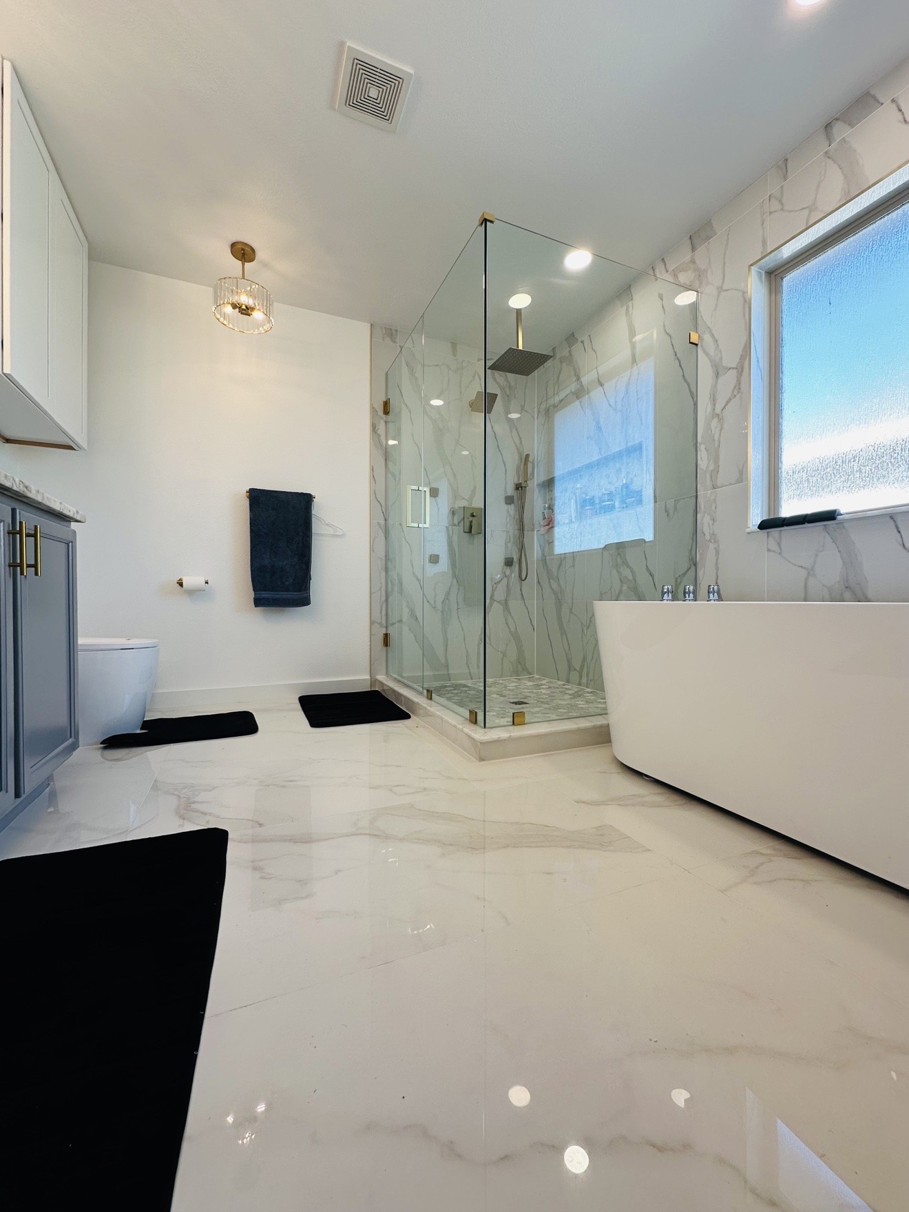White marble bathroom with frameless glass shower, freestanding tub, and vanity